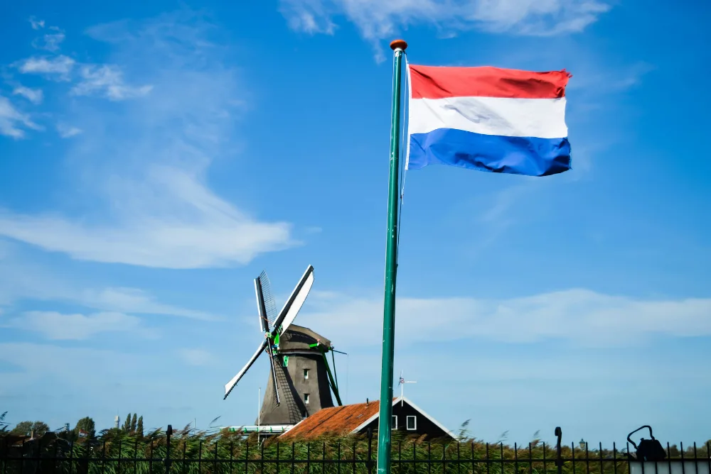The Dutch flag flying beside a windmill under a blue sky