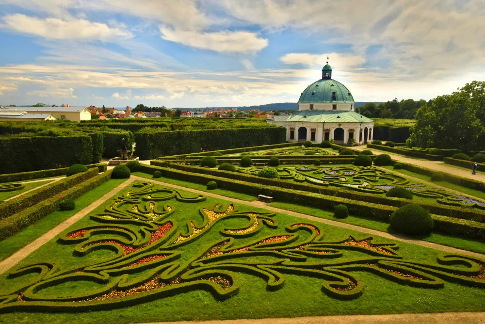 A formal baroque garden with clipped hedges leading to a domed pavilion