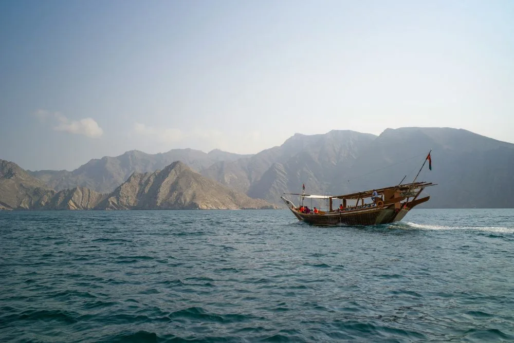 A traditional wooden dhow sailing past the coastal mountains of Oman