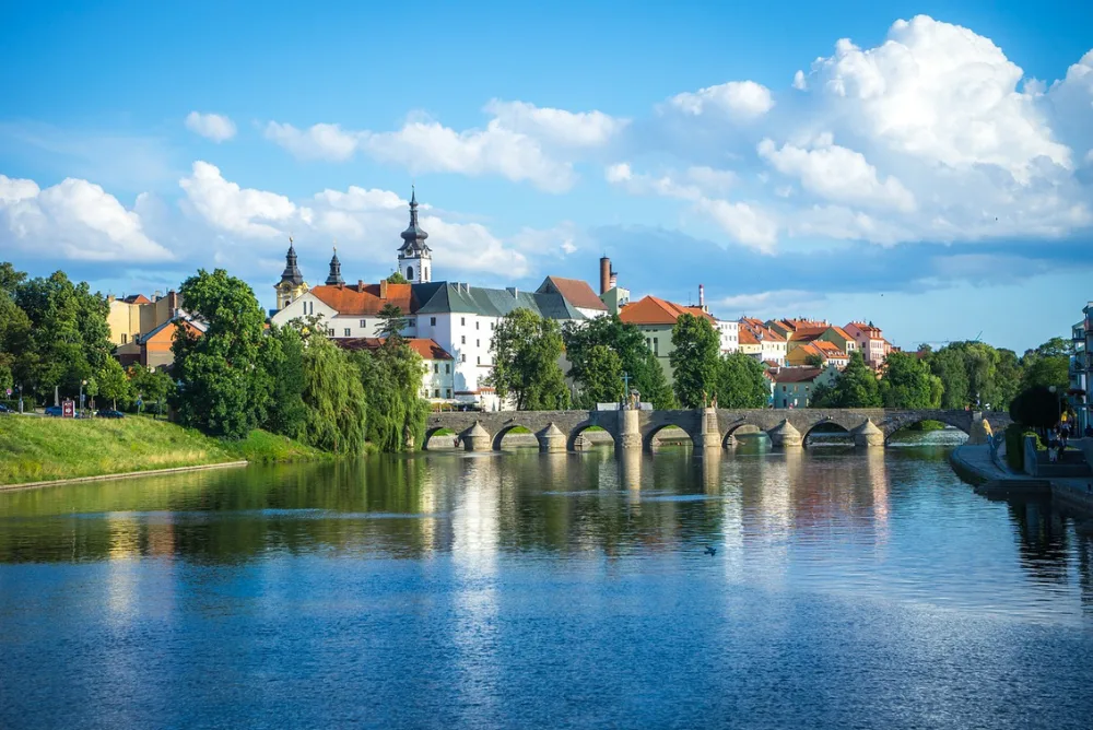A Czech riverside town with a stone bridge below a castle