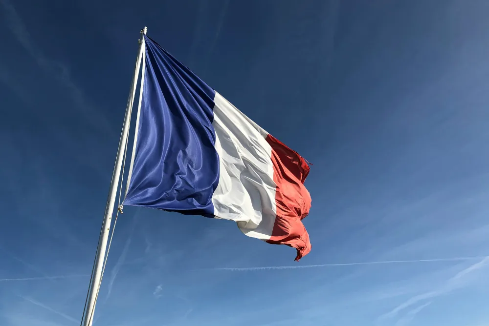 The French tricolour flying from a pole against a clear blue sky
