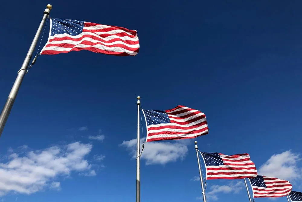 Three United States flags flying from poles against a blue sky
