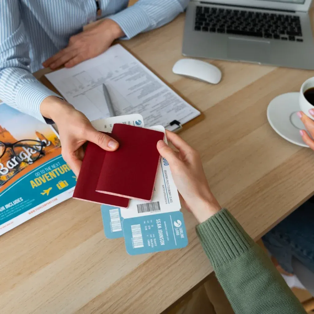 A passport being handed across a desk spread with travel documents